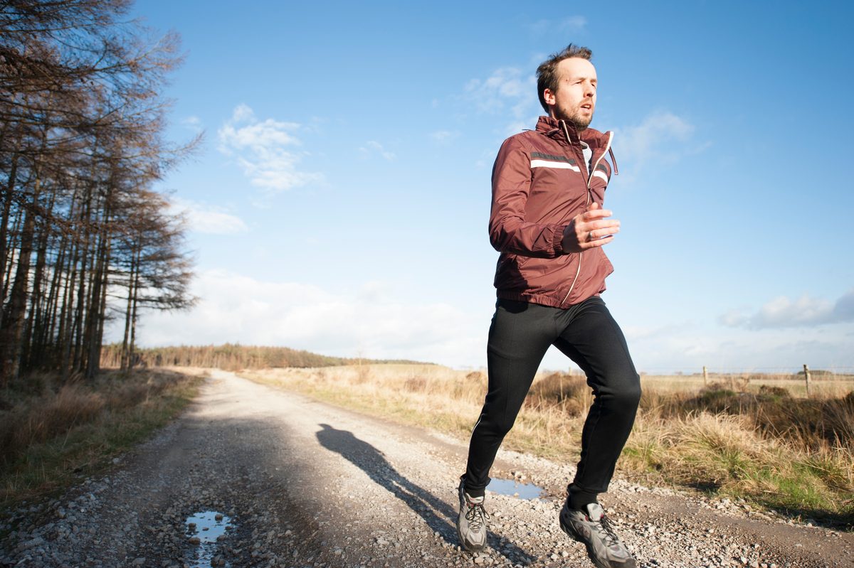Man running on a trail path with determination — continuing to train through manageable tendon discomfort